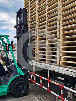 Worker driving forklift to loading and unloading wooden pallets from truck to warehouse cargo storage, shipment in logistics and