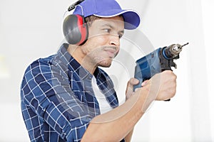 worker with electric drill perforator equipment making hole in wall