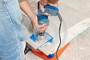 Worker with electric drill preparing tiles for installation indoors, closeup