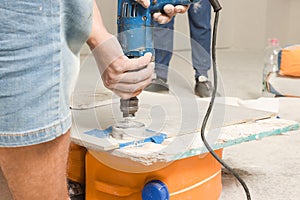 Worker with electric drill preparing tiles for installation indoors, closeup