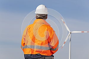 Worker or engineer with hard hat and protecive clothing looking at a windmill of a windfarm