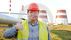 Worker or engineer looking directly at the camera and showing thumb up standing in front of a power station