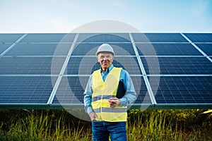 Worker or engineer stands front of solar panels looking at camera.