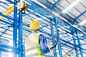 Worker in factory controlling crane with remote