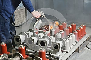 A worker at a factory in a special room paints parts of the valves from the spray gun. Paint valves in gray color, hand