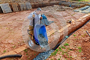 Worker fills drainage pipe with crushed stone from a wheelbarrow