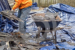 Worker fills wheel barrow with old shingles