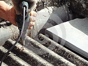 Worker fixing dirty old roof with electric drill screwdriver