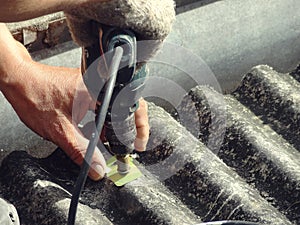 Worker fixing dirty old roof with electric drill screwdriver