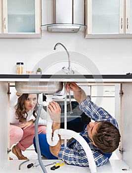 Worker Fixing Sink In Front Of Woman In Kitchen