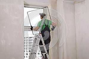 Worker on folding ladder installing window indoors, back view