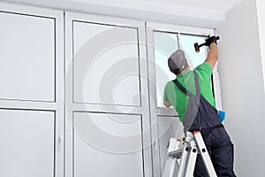Worker on folding ladder installing window indoors, back view