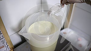 Worker at food factory pouring powdered sugar from scoop to a mixing bucket with cold cream for ice cream preparation