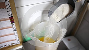 Worker at food factory pouring sugar from scoop to a mixing bucket with cold freshly squeezed orange juice for ice cream