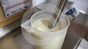 Worker at food factory preparing ice cream using a professional blender in a bucket mixing cold cream