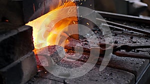 worker in forge tosses coal into furnace to heat iron. blacksmith in white cotton shirt and apron with fireproof gloves