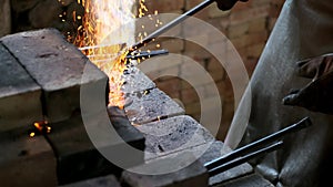 worker in forge tosses coal into furnace to heat iron. blacksmith in white cotton shirt and apron with fireproof gloves