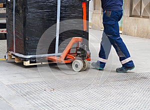 Worker with fork pallet truck stacker in warehouse loading furniture panels