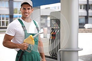 Worker with fuel pump nozzle at modern gas station