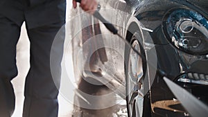 Worker in garage automobile service is washing a car in the suds by water hoses, detail close up