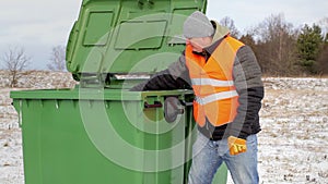 Worker with garbage bags near the container in winter