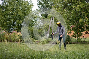 Worker with a gas mower in his hands, mowing grass in front of the house. Trimmer in the hands of a man. Gardener cutting the