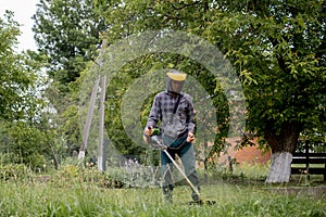 Worker with a gas mower in his hands, mowing grass in front of the house. Trimmer in the hands of a man. Gardener cutting the