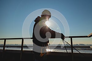 Worker in gear in the rays of the bright sun on the roof of a high-rise building pulls a climbing rope