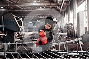 Worker girl with welding on steel structure in factory, light spark