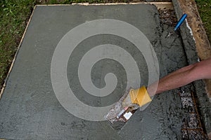 Worker gloved hand smoothing fresh concrete foundation