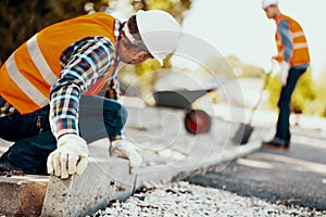 Worker with gloves and in a helmet arranging curbs on the street