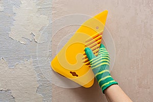 A worker glues wallpaper with a spatula onto an unprepared wall. The concept of repairing a house or apartment