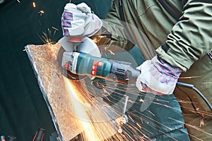 Worker grinding cutting metal sheet with grinder machine and sparks