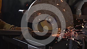 Worker is grinding edge of metal beam by disk of polishing machine in factory