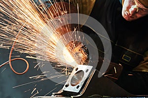 Worker grinding weld seam with grinder machine and sparks