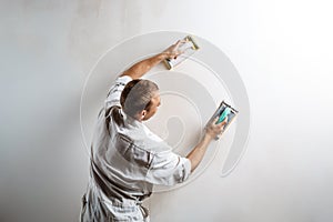 Worker grinding white wall with sandpaper. Copy space.