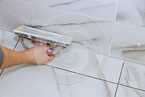 Worker grouting tiles with trowel cement mortar