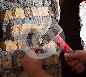 worker with a hammer and chisel makes a hole in the wall at the construction site