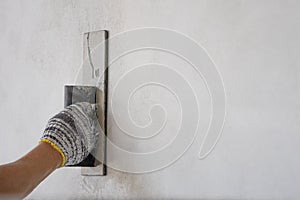 worker hand with glove holding trowel is plastering cement wall