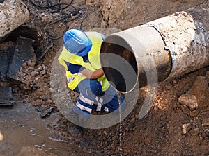 Worker with hand grinder cut metal tube. Sparks are flying down to wet clay. Working staff in safety clot