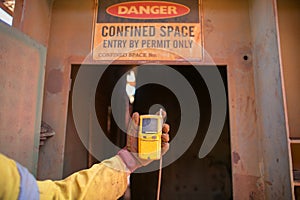 Worker hand holding gas test detector device while commencing safety gas testing atmosphere at main entry and exit on confined spa