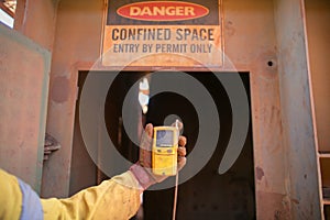 Worker hand holding gas test leak detector device at main confined space entry and exit photo