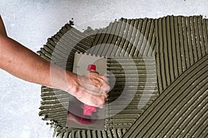 Worker hand with trowel tool for tiles installation making mortar adhesive on floor