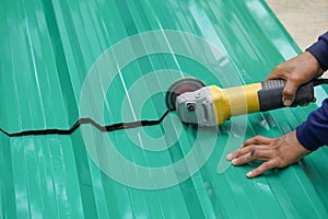 Worker hands cutting a metal sheet for roofing by using an angle grinder on the floor