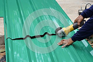 A worker hands cutting a metal sheet for roofing by using an angle grinder on the floor