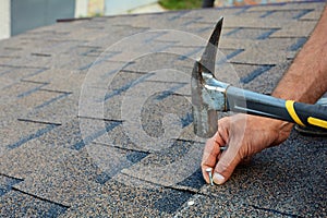 Worker hands installing bitumen roof shingles. Worker Hammer in Nails on the Roof. Roofer is hammering a Nail in the Roof Shingles