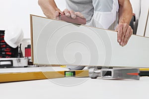Worker hands installing timber laminate white floor. Precise finishing using sandpaper. Wooden floors house renovation photo