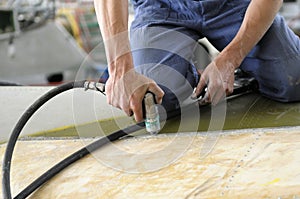 Worker hands making holes with a pneumatic drill on the body plane for further riveting photo