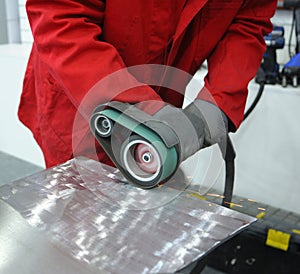 Worker hands sanding metal sheet by the hand held belt sender