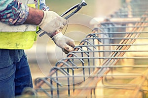 Worker hands using steel wire and pliers to secure bars on construction site